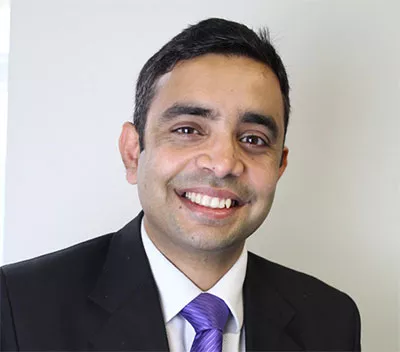 Ikhlaq Hussain, smiling and wearing a purple tie