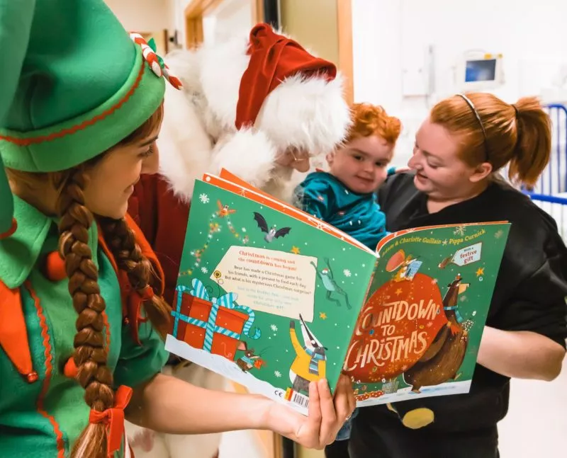 GOSH patient reads a story with GOSH volunteer elves and Father Christmas