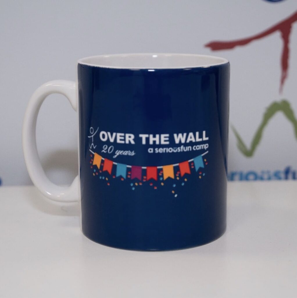 Blue mug on table, with 'Over The Wall. A serious fun camp' text on it, with a row of flags or bunting. Marking the charity's 20th anniversary.. Photo: Over The Wall