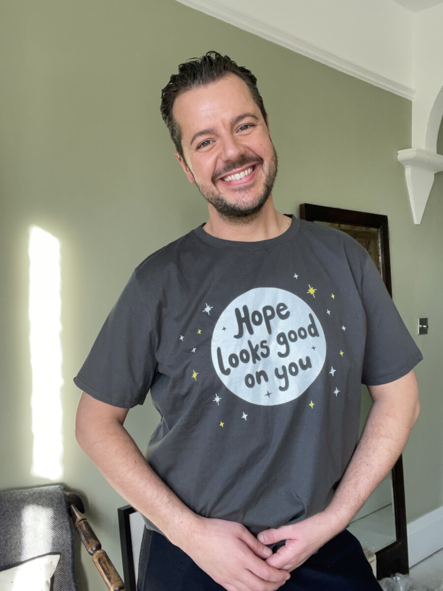 Jules von Hep smiles as he wears a t-shirt he has designed for Young Lives vs Cancer & World Cancer Day