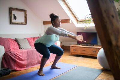 a black woman in sports gear does squats in her living room