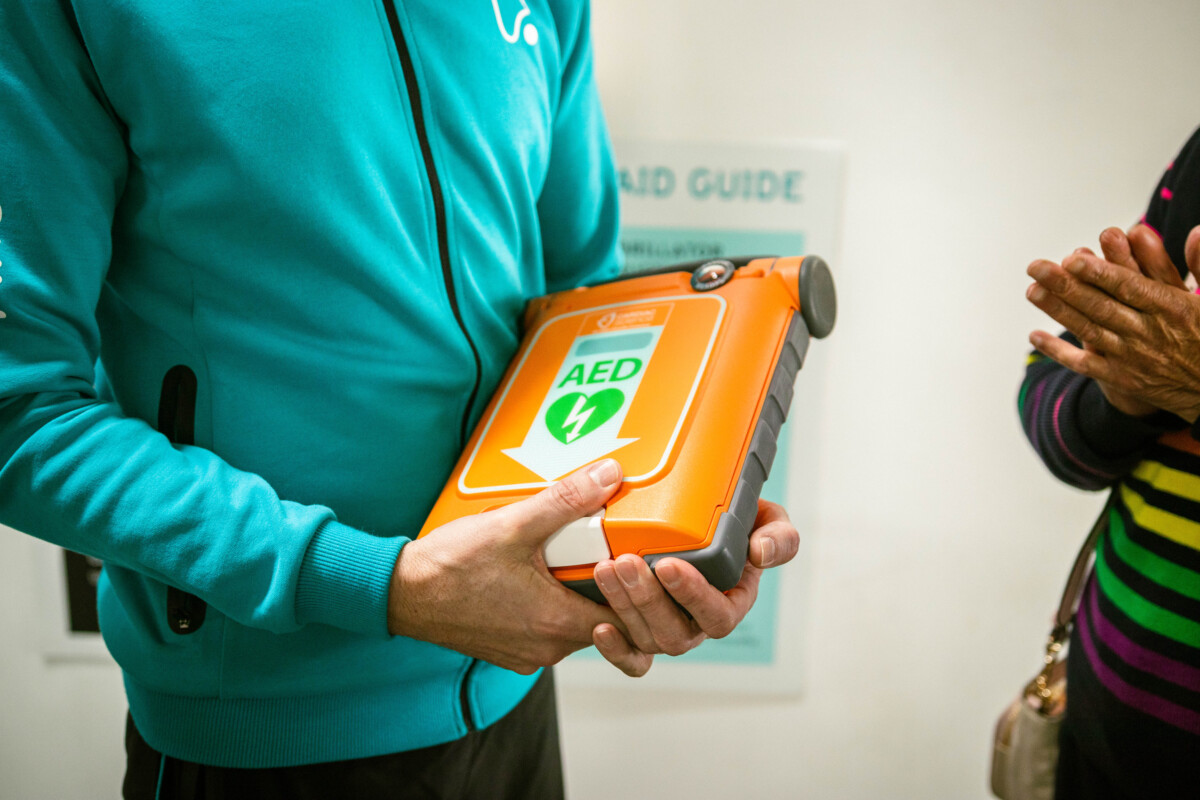 A person in a teal coloured top holds an orange defibrillator