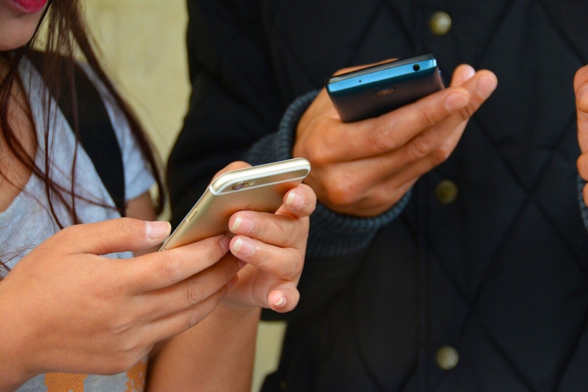 two people stand side by side, phones in hand