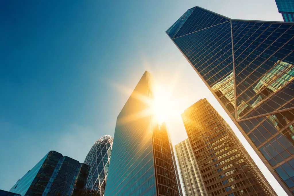 View looking up to sun behind city skyscrapers and a blue sky