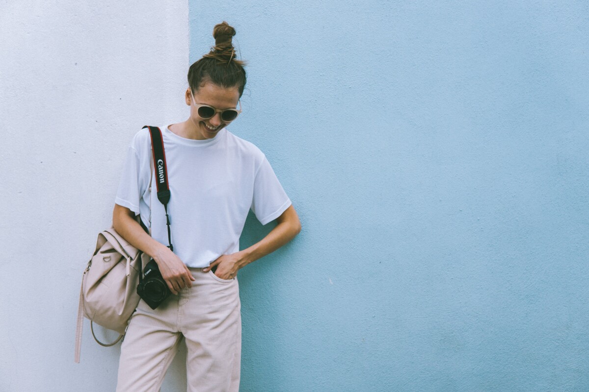 A woman with sunglasses dressed in casual clothes, with a Canon camera over her shoulder.
