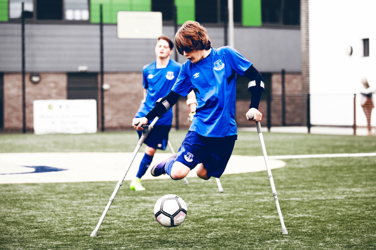 Two young players in football kit and on crutches from The People's Hub. ©Stella Pictures Limited