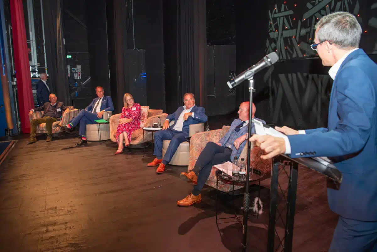 Angels Den 2024. Five Angels sit in arm chairs on a stage, next to a master of ceremonies