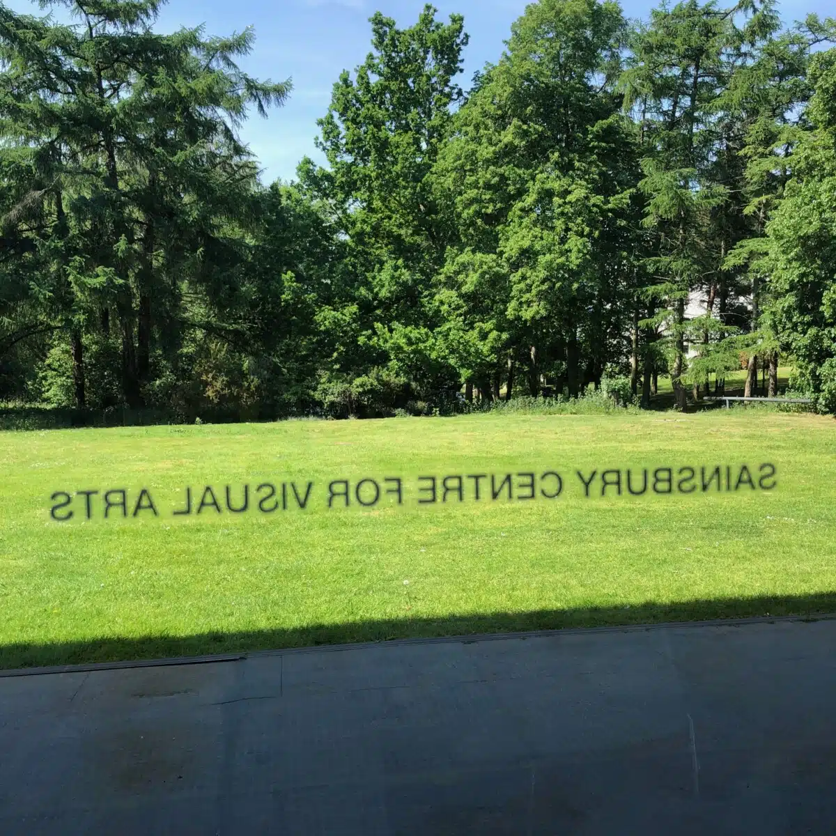 Sainsbury Centre for Visual Arts, UEA. Building name seen in reverse through a glass window, looking out onto grass and trees from the building's cafe.