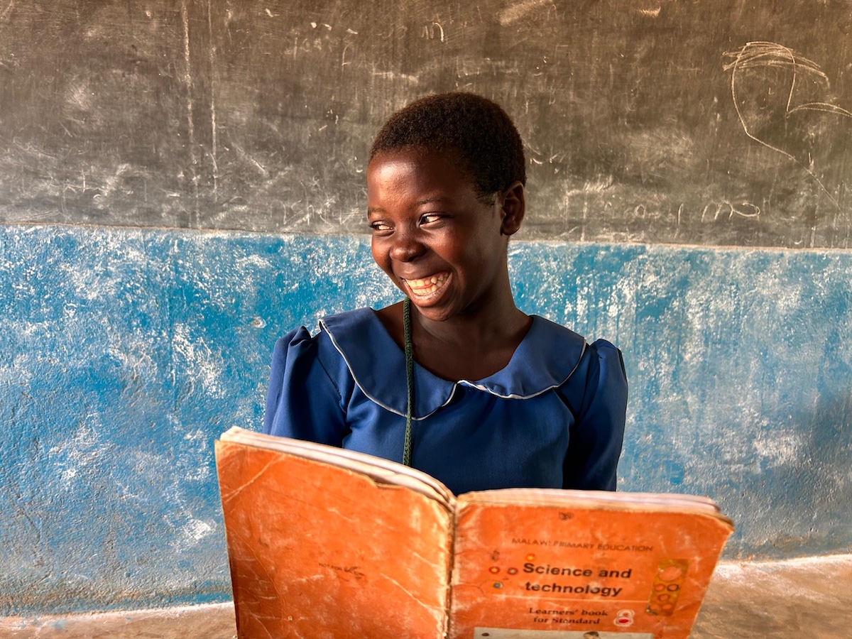 Elise in a Malawi school, smiles, holding a Science and Technology school book. Photo: Mary's Meals